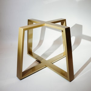 May include: Gold metal table base with a cross-shaped design. The base is made of thick metal and has a polished finish.