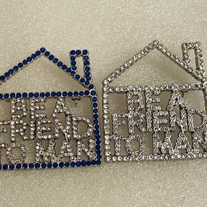 May include: Two house-shaped brooches. One is outlined in blue stones with the words "BE FRIEND TO MAN" in clear stones. The other brooch is outlined in clear stones with the same text in clear stones.