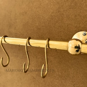 Peut inclure: Crémaillère de cuisine en métal doré avec quatre crochets. La crémaillère est fixée au mur et a un embout rond.