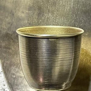 May include: A gold metal candle holder with a round, fluted cup. The holder has a simple, elegant design.