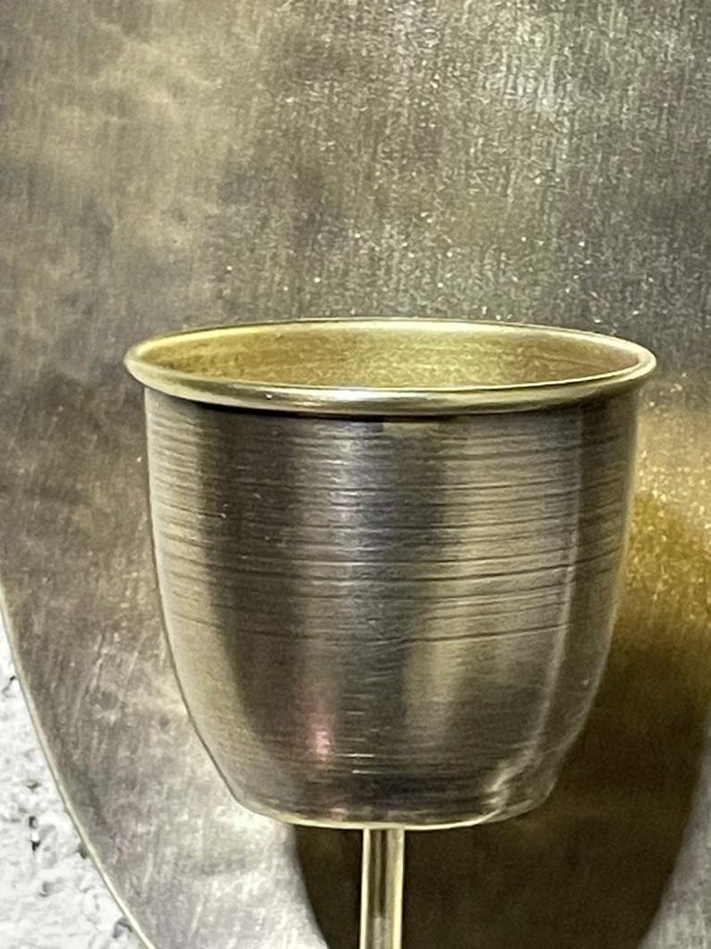 May include: A gold metal candle holder with a round, fluted cup. The holder has a simple, elegant design.