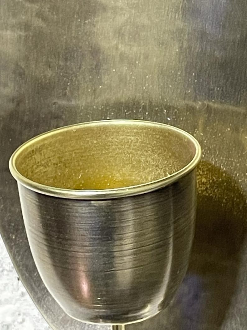 May include: A gold-colored metal cup with a smooth, shiny surface. The cup is empty and has a slightly rounded shape.