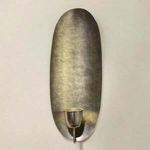 May include: A silver oval wall sconce with a single candle holder. The sconce has a textured surface and a simple design.