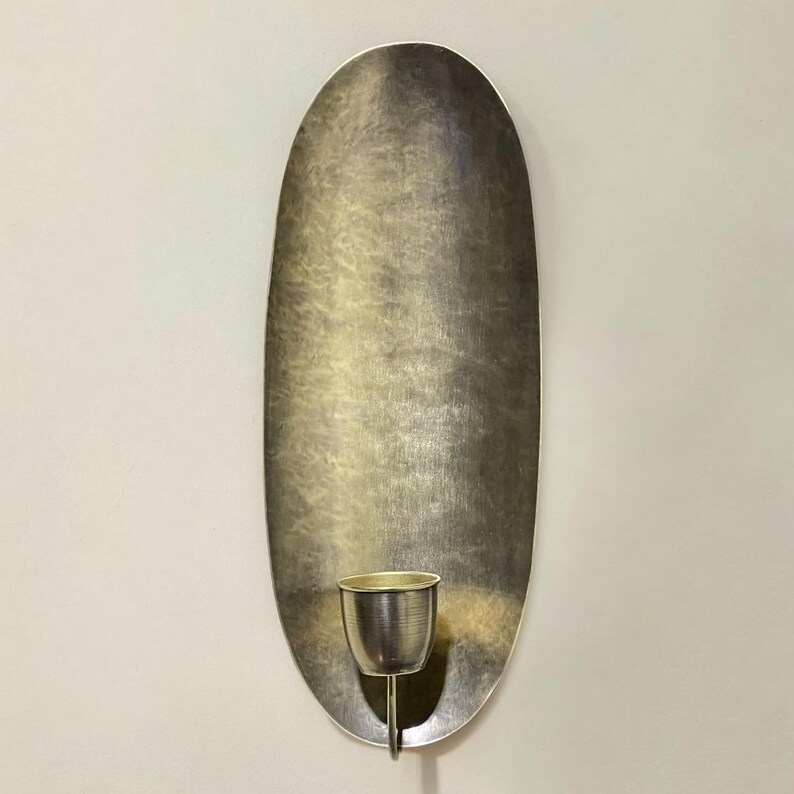 May include: A silver oval wall sconce with a single candle holder. The sconce has a textured surface and a simple design.