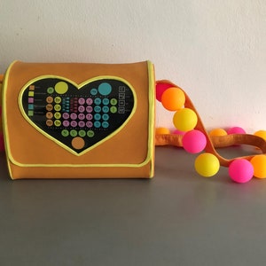 May include: A bright orange purse with a heart-shaped flap featuring a periodic table of elements. The purse has a bright yellow strap with a string of colorful balls.