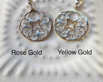 Puede incluir: Se muestran dos colgantes circulares de filigrana, uno en oro rosa y otro en oro amarillo. Cada colgante presenta un diseño calado con una flor central de cuatro pétalos. Los colgantes están etiquetados como "Rose Gold" y "Yellow Gold".