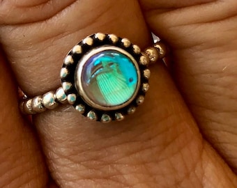 Puede incluir: Un anillo de plata con una piedra preciosa redonda azul iridiscente engastada en un engaste de cuentas.