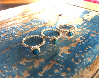 Puede incluir: Tres anillos plateados con un diseño de cuentas y una piedra turquesa. Los anillos se exhiben sobre una superficie de madera pintada de azul desgastado. Los anillos están enfocados, mostrando los detalles de la joyería.