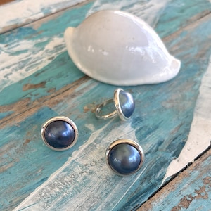 May include: A set of three silver rings with dark blue pearl-like stones. The rings are on a wooden surface with a white seashell.