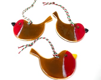 May include: Three brown glass robin ornaments with red and white accents and a yellow beak. Each ornament has a red and green twine string for hanging.