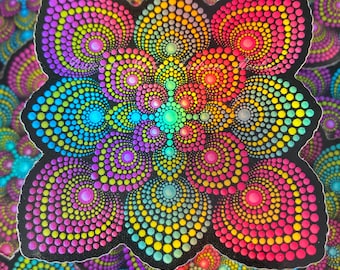 May include: A colorful sticker with a mandala design made of small dots in shades of pink, blue, green, and yellow. The sticker is on a black background and has a slightly irregular shape.