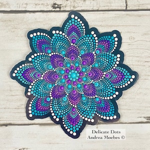May include: A teal and purple mandala sticker with a black background. The mandala is made up of small dots and has a swirling pattern. The sticker says "Delicate Dots Andrea Moebes ©" at the bottom.
