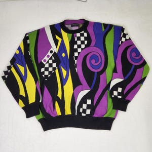 May include: A long-sleeve crewneck sweater featuring a bold, abstract graphic pattern in vibrant shades of purple, lime green, yellow, and blue, accented with black and white checkerboard sections and solid black ribbed cuffs and hem.