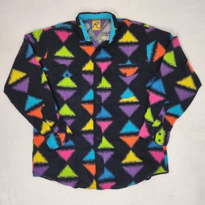 May include: A long-sleeve button-up shirt in black featuring a repeating geometric pattern of triangles in neon pink, yellow, purple, orange, and blue. The shirt includes a collar, two chest pockets with flaps, and buttons on the cuffs.