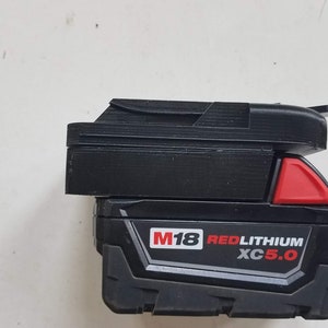 May include: A black and red Milwaukee M18 REDLITHIUM XC 5.0 battery pack.