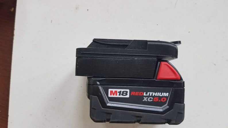 May include: A black and red Milwaukee M18 REDLITHIUM XC 5.0 battery pack.