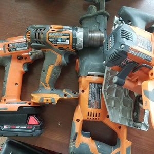 May include: Four orange and black cordless power tools, including a drill, a saw, a hammer drill, and a reciprocating saw. The tools are on a wooden surface.