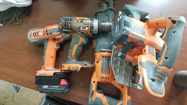 May include: Four orange and black cordless power tools, including a drill, a saw, a hammer drill, and a reciprocating saw. The tools are on a wooden surface.