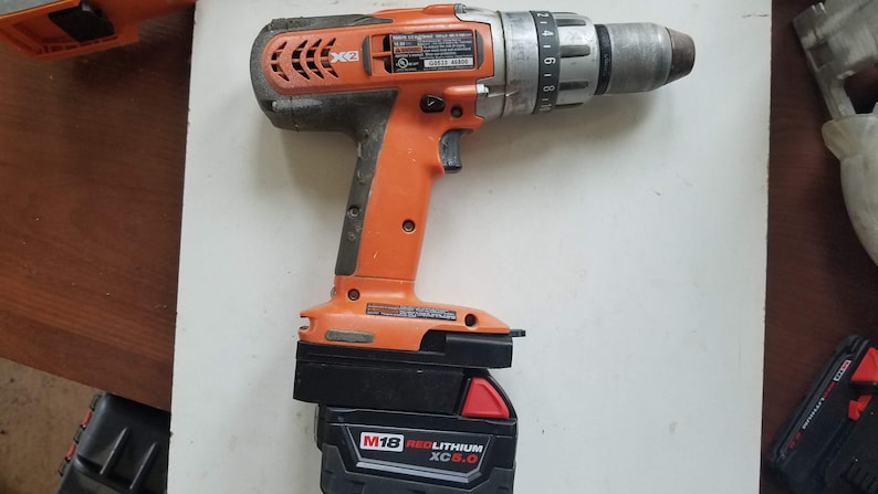 May include: An orange and black cordless drill with a black and red battery pack. The battery pack has the text "M18 REDLITHIUM XC 5.0" on it.