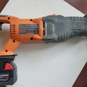 May include: An orange and black cordless reciprocating saw with a black battery pack labeled "M18 RED LITHIUM XC 6.0" and the brand name "RIDGID" on the saw.