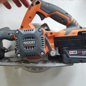 May include: An orange and black cordless circular saw with a 7-1/4 inch blade. The saw has a black battery pack labeled "M18 REDLITHIUM XC5.0" and a black and orange handle. The saw is made by RIDGID.