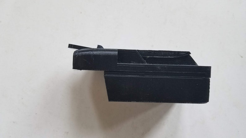 May include: A black plastic 3D printed object with a rectangular shape and a small, angled flap on the top.
