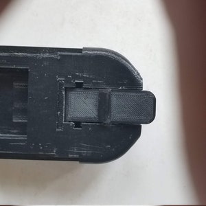 May include: Black plastic battery adapter with a latch on the side.