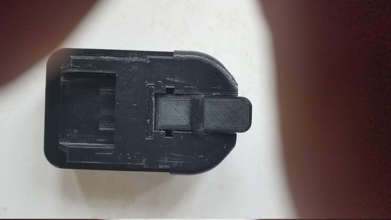 May include: Black plastic battery adapter with a latch on the side.
