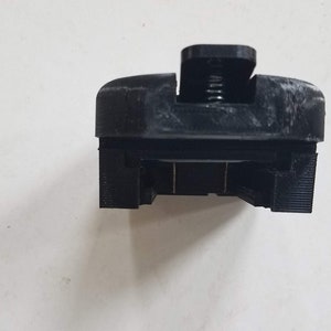 May include: Black plastic 3D printed object with a spring and a slot for a phone or other device.