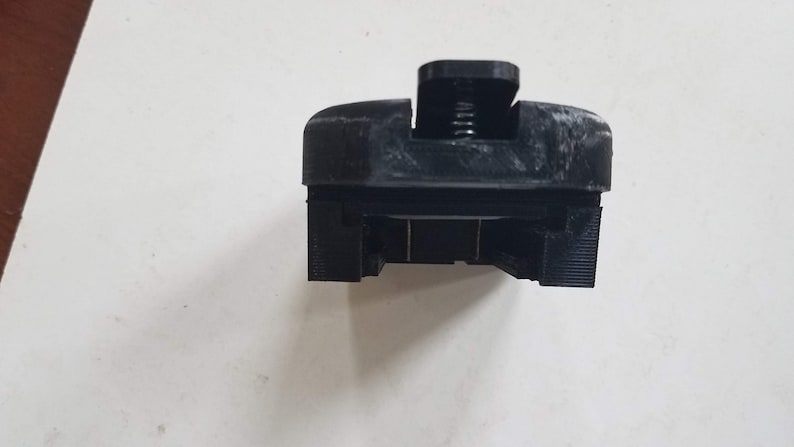 May include: Black plastic 3D printed object with a spring and a slot for a phone or other device.