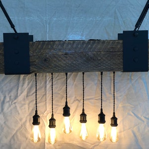 May include: A rustic wooden beam chandelier with six black pendant lights and Edison bulbs. The beam is attached to the ceiling with black metal brackets.