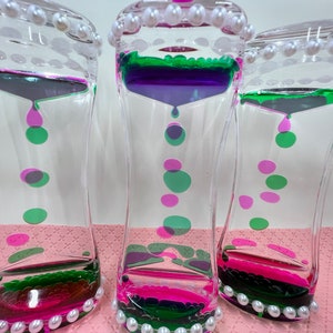 May include: Three clear glass hourglass-shaped liquid timers with pink, green, and purple liquid. Each timer has a pearl trim around the top and bottom.