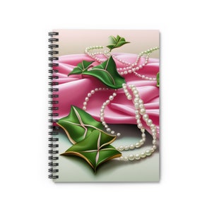 May include: Two green leaves with gold accents are arranged on a pink satin fabric with two strands of white pearls.