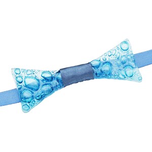 May include: A blue glass bow tie with a textured bubble design. The bow tie is tied with a dark blue ribbon.
