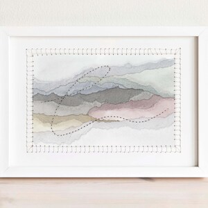 May include: A framed abstract watercolor painting with stitched edges. The painting features layers of soft, muted colors in shades of gray, blue, pink, and beige. The stitching creates a textured effect and adds a unique touch to the artwork.