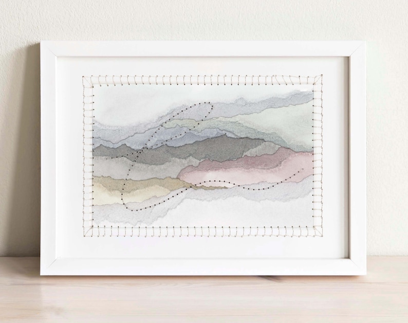 May include: A framed abstract watercolor painting with stitched edges. The painting features layers of soft, muted colors in shades of gray, blue, pink, and beige. The stitching creates a textured effect and adds a unique touch to the artwork.