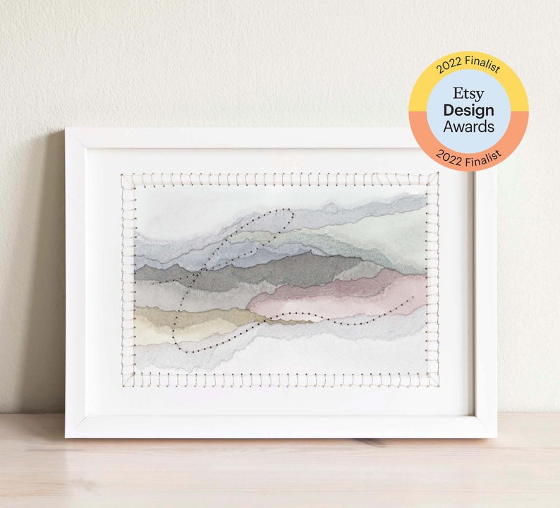 May include: A framed watercolor painting of abstract landscape with stitched edges. The painting features shades of gray, beige, and pink. The frame is white. The image includes the text "2022 Finalist Etsy Design Awards 2022 Finalist".