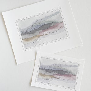 May include: Two watercolor paintings of abstract landscapes with stitched borders. The paintings are in shades of gray, brown, and pink. The smaller painting is on top of the larger painting.