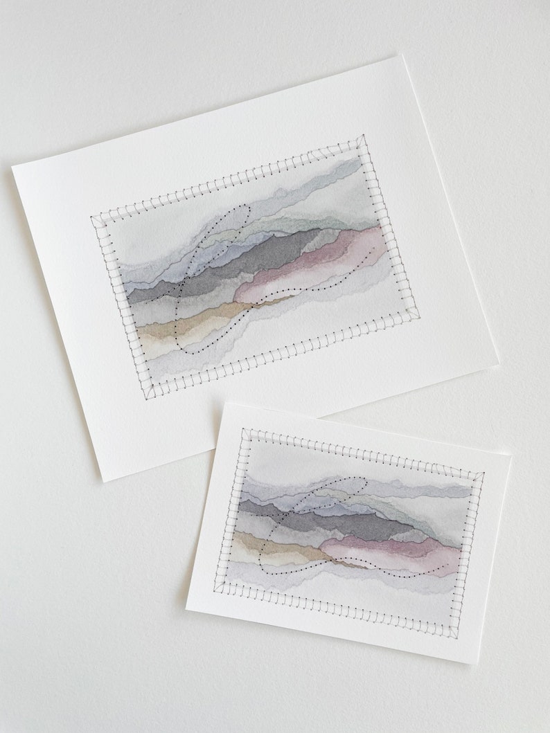 May include: Two watercolor paintings of abstract landscapes with stitched borders. The paintings are in shades of gray, brown, and pink. The smaller painting is on top of the larger painting.