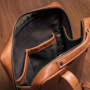 K&ouml;nnte beinhalten: Ein brauner Lederrucksack mit Rei&szlig;verschluss und einem gro&szlig;en Fach im Inneren. Der Rucksack hat zwei verstellbare Tr&auml;ger.