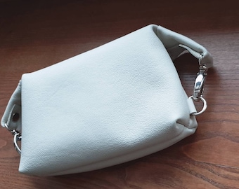 May include: A white leather handbag with a silver chain strap and a silver clasp.