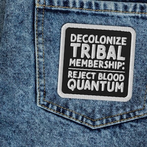 May include: A pair of blue denim jeans with a black and white patch on the back pocket. The patch reads "Decolonize Tribal Membership: Reject Blood Quantum".