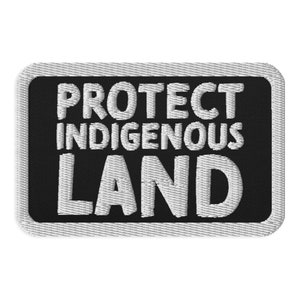 Könnte beinhalten: Schwarzer und weißer gestickter Aufnäher mit dem Text "PROTECT INDIGENOUS LAND" in weißen Buchstaben.