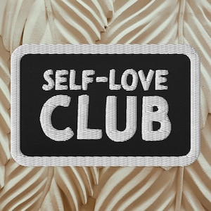 Könnte beinhalten: Schwarzer gestickter Aufnäher mit weißen Nähten. Der Aufnäher zeigt "SELF-LOVE CLUB" in einer fetten, verspielten Schrift.