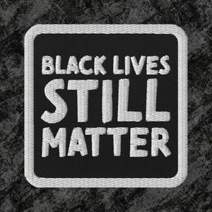 May include: Black and white embroidered patch with the text "Black Lives Still Matter" on a black background.