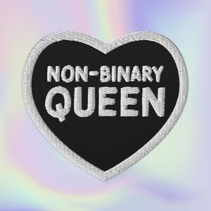 Könnte beinhalten: Schwarzer herzförmiger Patch mit weißen Nähten an den Rändern. Der Text "NON-BINARY QUEEN" ist in Weiß auf den Patch gestickt.
