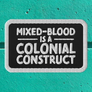 Op de afbeelding: Een zwarte geborduurde patch met witte stiksels met de tekst "Mixed-Blood is a Colonial Construct."