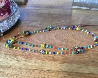 May include: A multi-strand necklace with colorful glass beads. The beads are a mix of small round beads and larger, more intricate beads with a variety of colors and patterns.