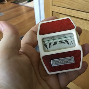 May include: A white and red light meter with a black dial and the text "Mini Rex-II" and "f/5.6".