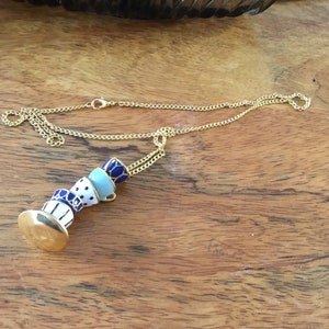 May include: A gold chain necklace with a pendant of stacked blue and white teacups. The teacups are decorated with gold trim and blue and white polka dots.